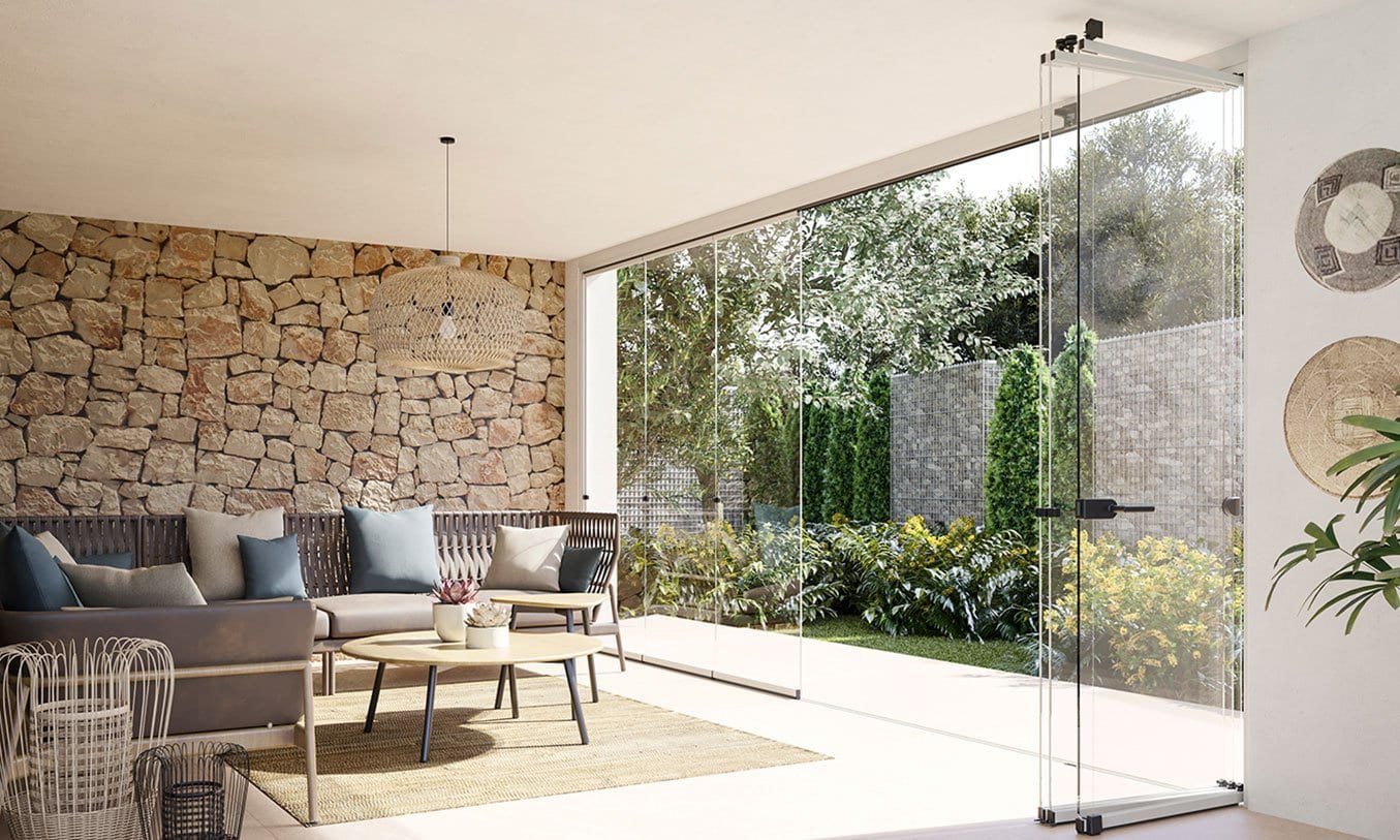 Porche con cortinas de cristal plegables abiertas hacia el jardín, con sofá y pared de piedra